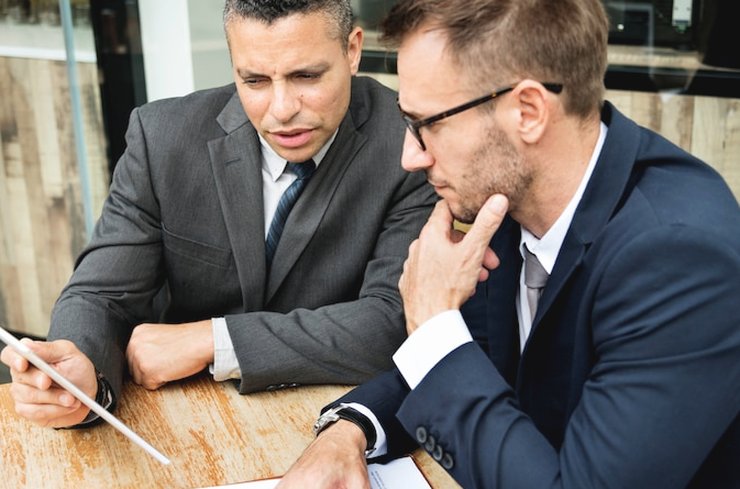 Two men in business clothes discussing a document at a wooden table