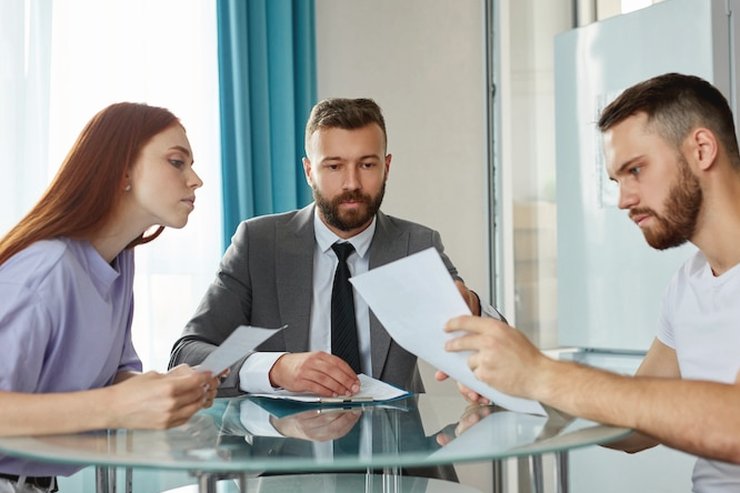 Three people around a glass table reading printed pages together
